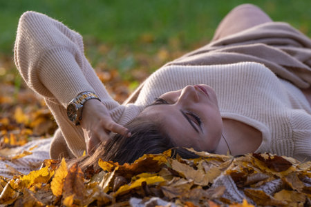 Autumn Walk. Female portrait. A happy girl lies with her eyes closed on the ground in a park among yellow leaves; side view, rear viewの写真素材