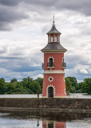 Pink lighthouse against the backdrop of dark thunderclouds. A man looks through binoculars, watches birds before a thunderstorm. Near Moritzburg Castle, Germanyの写真素材