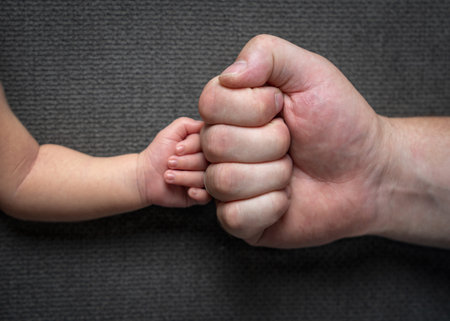 Big daddy's fist and newborn baby's fist on a gray background. Father's care and loveの写真素材