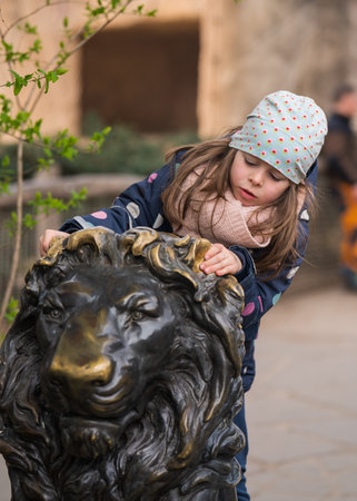Cute little girl sits on bronze lion at zoo. Active vacation. Family day.の写真素材