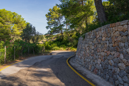 Quiet asphalt road running alongside traditional stone wall, surrounded by scenic Mediterranean...
