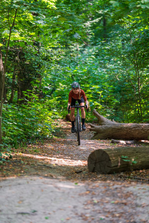 Young woman in professional cycling uniform rides gravel bike on forest trail on sunny day. Active...