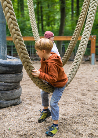 Boy having fun outdoor. Child hanging on rope swing in park.の写真素材
