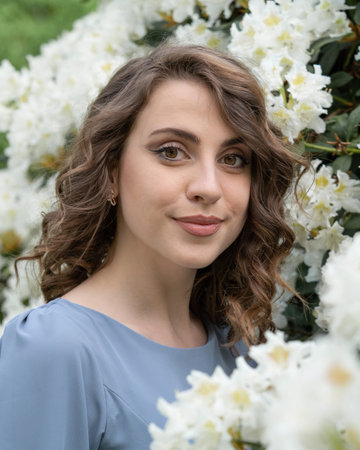 Beautiful young girl among white flowers of rhododendrons.