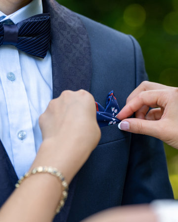 Hands of the bride close up. The bride adjusts the scarf on the groom's jacket. The groom dresses...