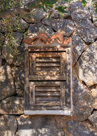 Old, small window with wooden shutters, blinds in a wall made of large stoneの写真素材
