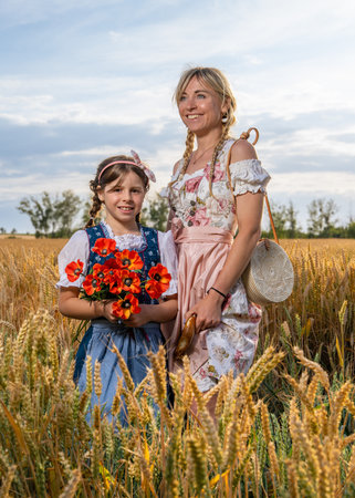 Traditional Bavarian mother and daughter enjoying time together in wheat field. Bright, joyful image of family, heritage, countryside life.の写真素材