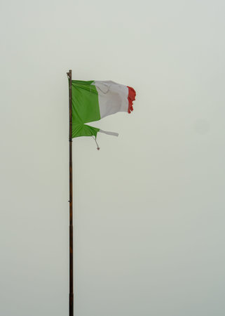 Worn Italian flag in Dolomites mountains surrounded by dense fog. Dramatic and mysterious atmosphere...