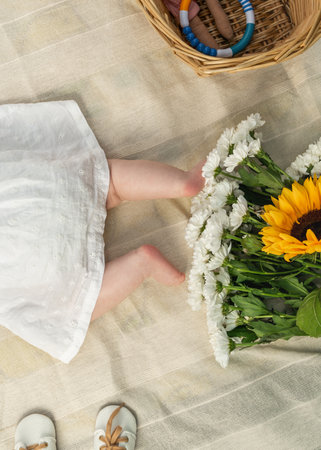Newborn baby girls legs resting on blanket, with baby booties, delicate flower bouquet nearby. Tender, heartwarming composition for baby announcements, parenting, maternity themes.の写真素材
