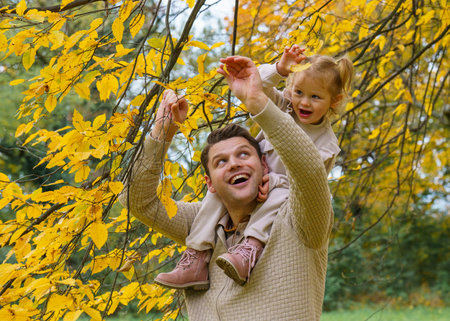 Joyful father and young daughter playing while walking in beautiful autumn park.Girl sitting on...