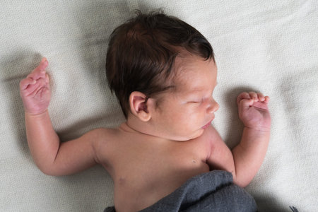 Portrait of a cute newborn baby boy under a white blanket. The kid raised his hands up