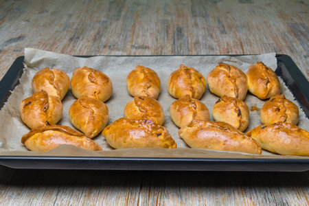 mini pies Pirozhki or piroshki on a cooking tray. Homemade baked yeast boat shaped buns with cabbage fillings. Eastern Europe food.の写真素材