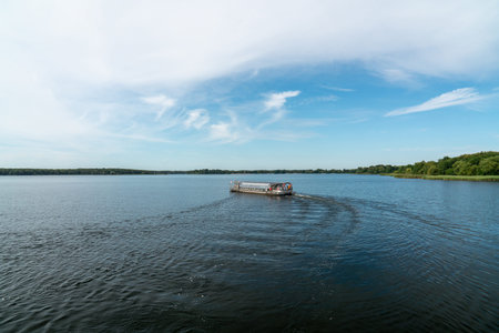 A tourist boat sails on a lake. Calm water. Green forests on the coast. Blue sky
