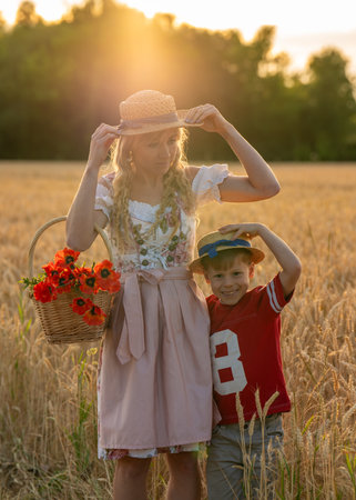 Little boys and mother in traditional Bavarian clothing stand together in wheat field at sunset, adjusting their hats. Happy family.の写真素材