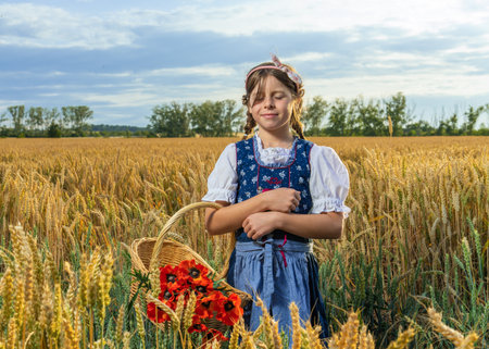 Child in folk Bavarian dress stands in wheat field with basket of poppies. Celebrating nature, cultural heritage, simple rural lifestyle.の写真素材