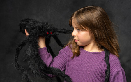 Portrait of cute little girl with large black spider on her hand against a dark background. Ideal for thematic portraits.の写真素材
