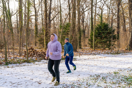 Happy middle aged man and woman jogging together in winter park. Active lifestyle, outdoor exercise, mental health, stress relief and wellbeing.の写真素材