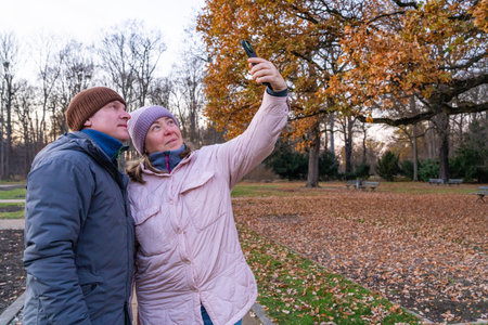 Happy middle aged couple taking selfie while walking in an autumn park. Concept of love, lifestyle, leisure, travel, relationships.の写真素材