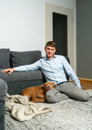 Man spending quiet time at home, softly stroking his American Staffordshire Terrier puppy. Cozy lifestyle moment highlighting affection, connection between pet owner and dog.の写真素材