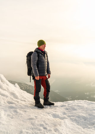 Male traveler with backpack standing on snowy peak Snezka mountain, enjoying winter landscape,...