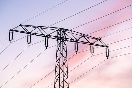 High voltage power lines and transmission towers silhouetted against colorful sunset sky. Ideal for...