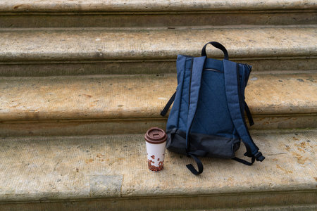 Backpack and reusable drink cup standing on outdoor stairs. Modern commuter lifestyle, mobility and daily routine concept.