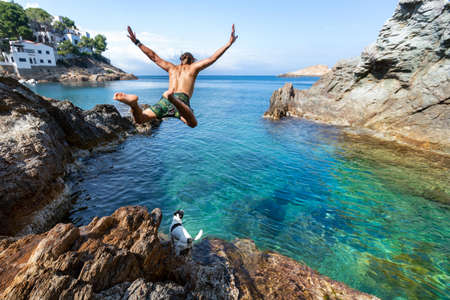 man jumping in to crystal mediterranean water with his dogの写真素材