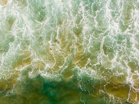 Aerial view of the sea with an emerald green color and large foaming waves