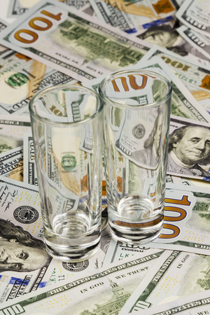 Two empty glasses stand next to each other on dollar billsの写真素材