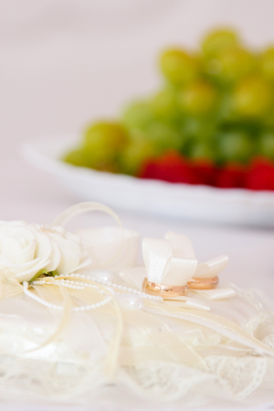 Gold wedding rings on wedding white cushion in the background plate with fruitsの写真素材