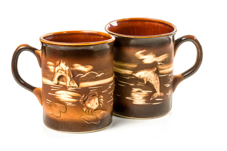 Two brown ceramic cups handmade ornament with sea gulls and dolphins crab isolated on white backgroundの写真素材