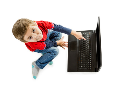 Little boy in red sweater and jeans sitting on floor and pointing to an open laptop top view isolated on white backgroundの写真素材