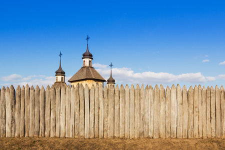 Wooden church with three steeples and crosses is behind a fence of logs against the skyの写真素材
