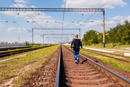 Woman with a handbag walking on railroad tracks away from the cameraの写真素材