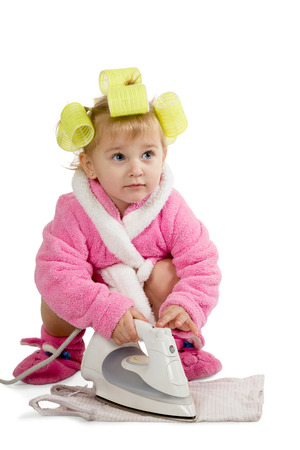 Little girl in a pink bathrobe and yellow curlers ironed his shirt on the floor isolated on white backgroundの写真素材