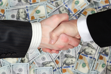 Handshake of two business men in suits on the background of hundred dollar bills stacked side by side in a random orderの写真素材