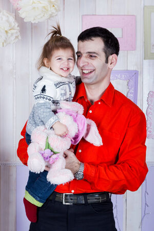 Happy dad in a red shirt holds on hands smiling daughter with a toy in the handsの写真素材