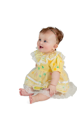 Portrait of little girl in a yellow dress sitting and looking sideways isolated on a white backgroundの写真素材