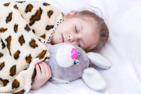 Little girl sleeping in an embrace with a toy hare under a blanket closeupの写真素材