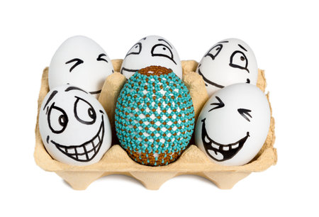 Easter egg decorated with beads standing among ordinary eggs with painted smiley faces isolated on a...