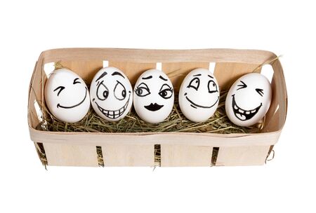 Eggs with painted smiling faces in a basket with hay isolated on white backgroundの写真素材