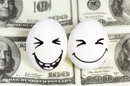 Two eggs with painted faces laughing at the a hundred dollar billの写真素材