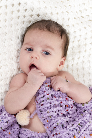 Newborn baby lying on a knitted blanket covered and holds his hand to his mouthの写真素材