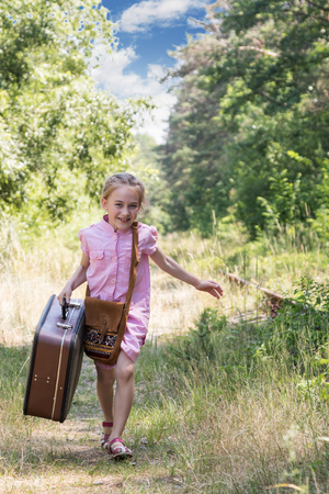 Girl in a pink dress with a suitcase in his hand running along the railway in the forestの写真素材
