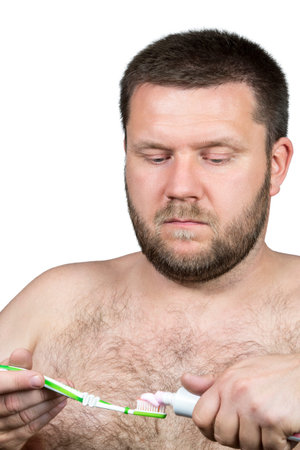 Serious man with a beard squeezed toothpaste on the brush to clean teeth isolated on white backgroundの写真素材