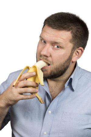 Bearded man in a blue shirt has bitten banana isolated on white backgroundの写真素材