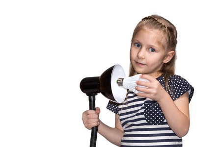 Little girl twists LED lamp into the luminaire closeup isolated on white backgroundの写真素材