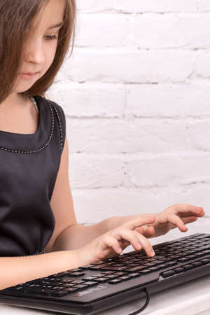 Girl in a black dress sitting and prints on the keyboard black closeupの写真素材