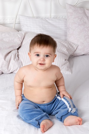 Portrait of sitting on bed a chubby baby in blue trousersの写真素材