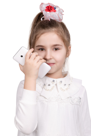 Half-length portrait of a little girl in a white dress with white smart phone in hand isolated on white backgroundの写真素材